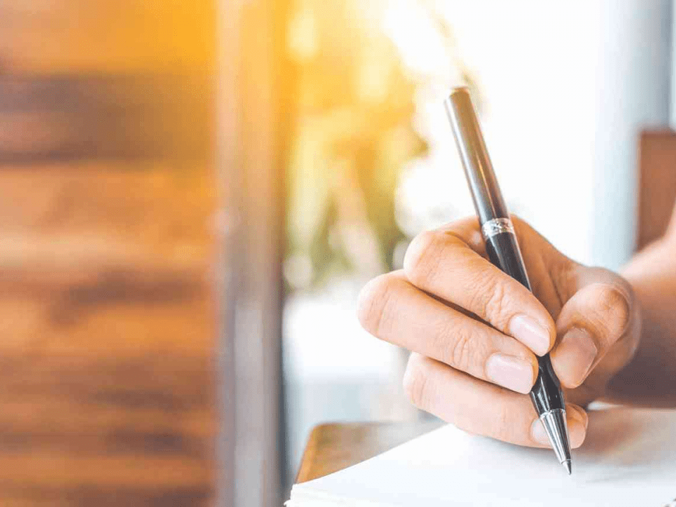 A person writing on paper with a pen.