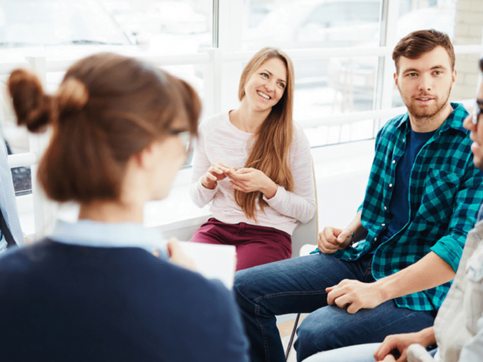 A group of people sitting in a room talking to each other